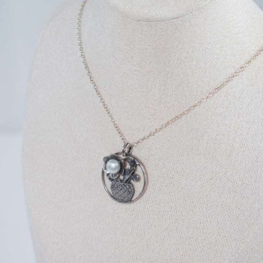 The Flower in the Basket pendant is a meticulously handcrafted antique silver masterpiece that exudes charm and elegance. Its intricate crisscross basket design cradles a delicate floral bloom, accented by a luminous pearl that adds a touch of sophistication.