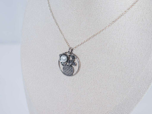 The Flower in the Basket pendant is a meticulously handcrafted antique silver masterpiece that exudes charm and elegance. Its intricate crisscross basket design cradles a delicate floral bloom, accented by a luminous pearl that adds a touch of sophistication.