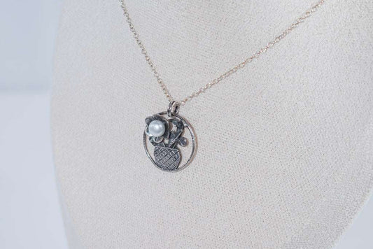 The Flower in the Basket pendant is a meticulously handcrafted antique silver masterpiece that exudes charm and elegance. Its intricate crisscross basket design cradles a delicate floral bloom, accented by a luminous pearl that adds a touch of sophistication.