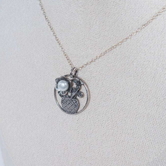 The Flower in the Basket pendant is a meticulously handcrafted antique silver masterpiece that exudes charm and elegance. Its intricate crisscross basket design cradles a delicate floral bloom, accented by a luminous pearl that adds a touch of sophistication.