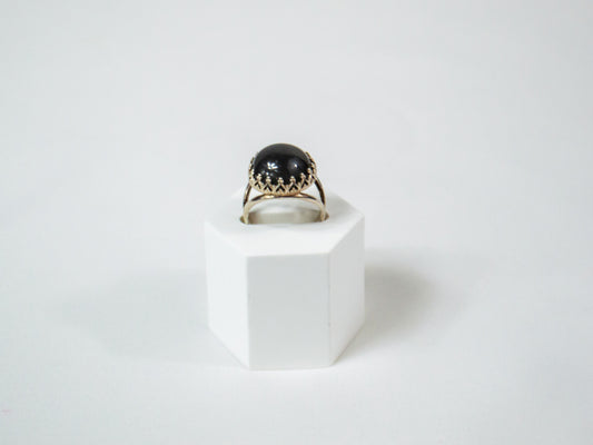 A delicate handcrafted sterling silver ring featuring a 14mm Grey Moonstone cabochon in a crown bezel setting, radiating a soft, ethereal glow.
