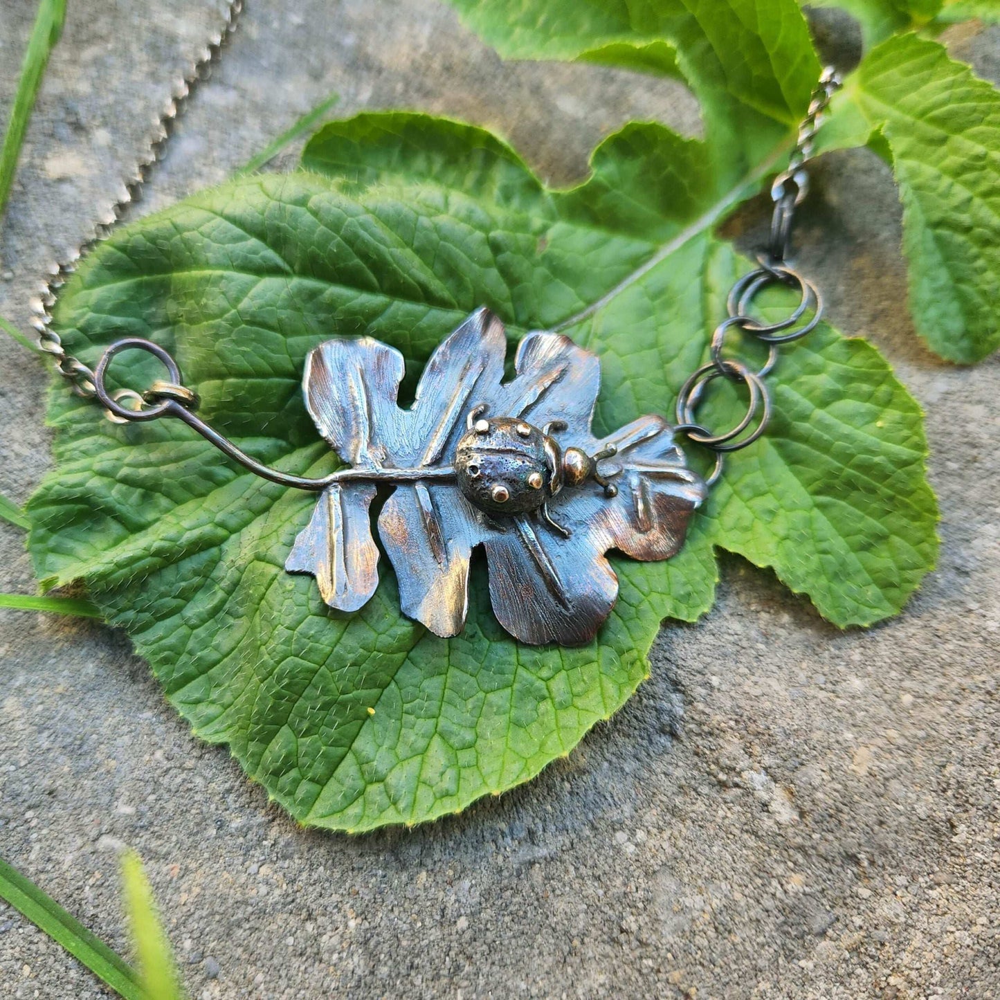 Handcrafted sterling silver pendant featuring a meticulously detailed ladybug resting on a textured, lifelike leaf. The design showcases expert metalwork, including fusing, reticulation, and soldering, finished with oxidation and polishing for depth and contrast. Paired with a handcrafted silver chain for a unique touch.