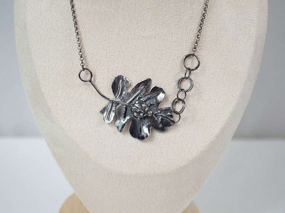 Handcrafted sterling silver pendant featuring a meticulously detailed ladybug resting on a textured, lifelike leaf. The design showcases expert metalwork, including fusing, reticulation, and soldering, finished with oxidation and polishing for depth and contrast. Paired with a handcrafted silver chain for a unique touch.