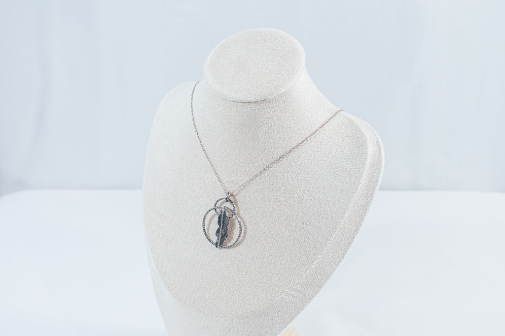 I textred pendant featuring two rings and a fern leaf in the center, hanging on a silver chain. Designed by Inga Rozin