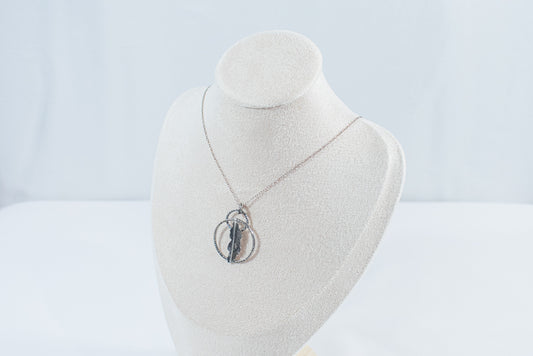I textred pendant featuring two rings and a fern leaf in the center, hanging on a silver chain. Designed by Inga Rozin