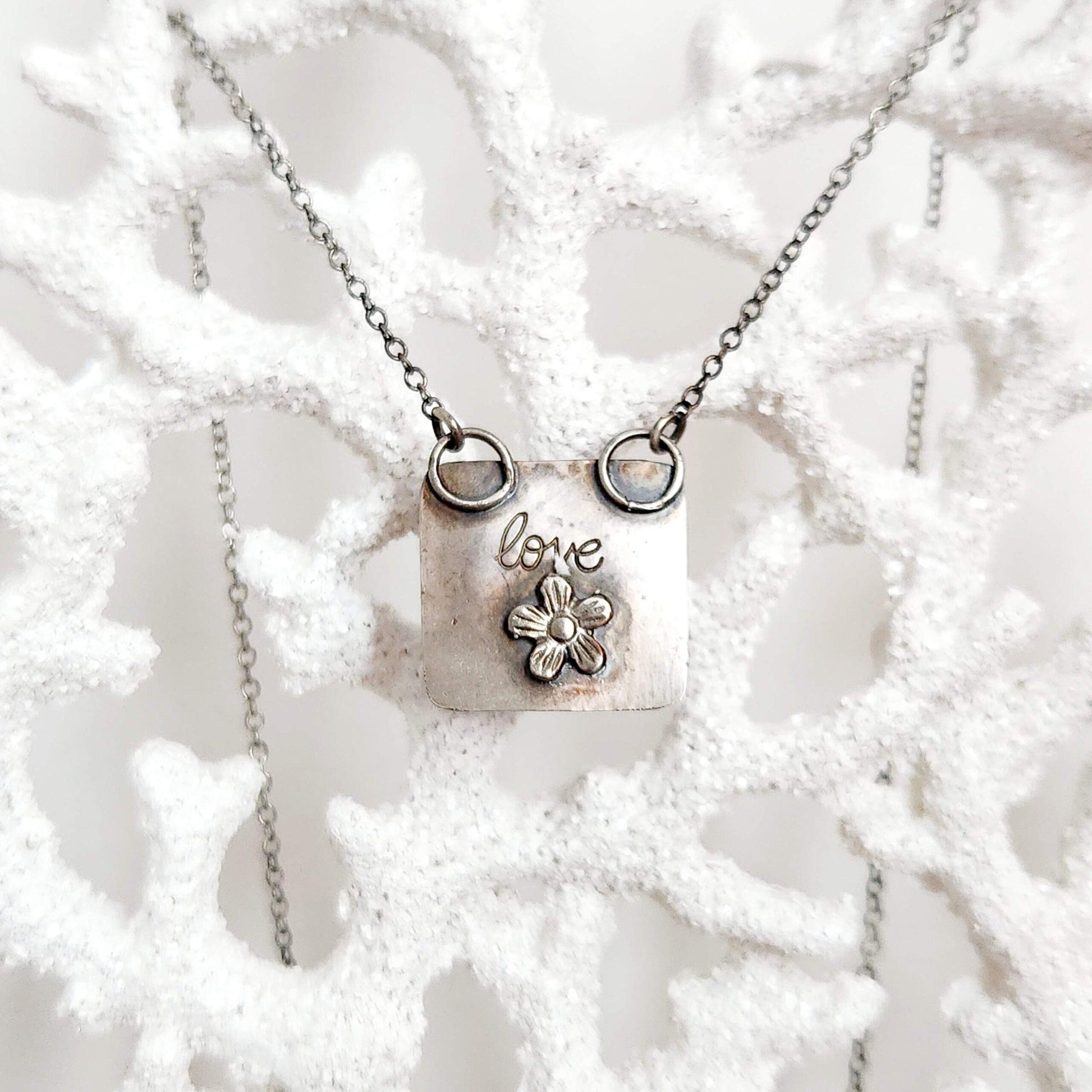 Heart-shaped pendant crafted from sterling silver and vibrant Rosarita Gold slag, featuring a radiant front and a back adorned with a delicate flower motif and the word 'LOVE.' A unique and timeless piece symbolizing warmth and affection.