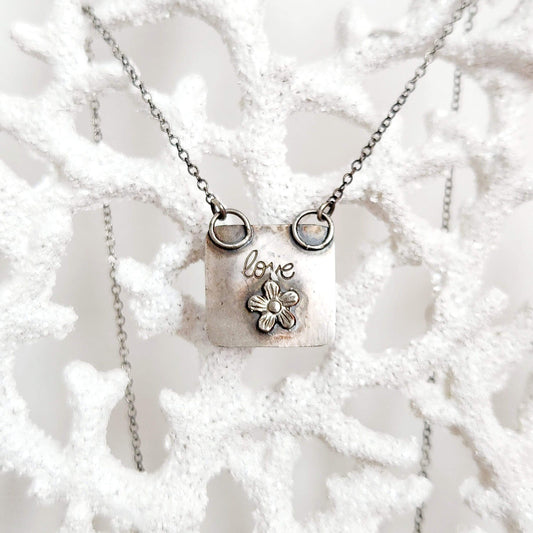 Heart-shaped pendant crafted from sterling silver and vibrant Rosarita Gold slag, featuring a radiant front and a back adorned with a delicate flower motif and the word 'LOVE.' A unique and timeless piece symbolizing warmth and affection.