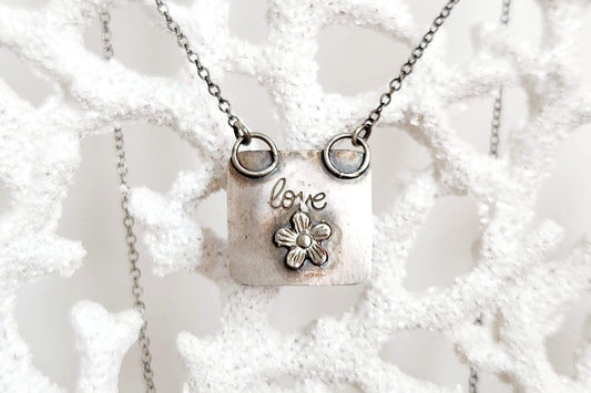Heart-shaped pendant crafted from sterling silver and vibrant Rosarita Gold slag, featuring a radiant front and a back adorned with a delicate flower motif and the word 'LOVE.' A unique and timeless piece symbolizing warmth and affection.
