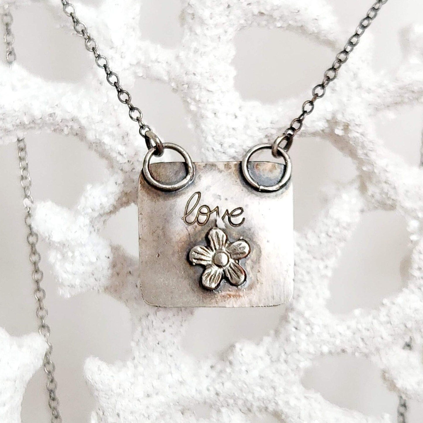 Heart-shaped pendant crafted from sterling silver and vibrant Rosarita Gold slag, featuring a radiant front and a back adorned with a delicate flower motif and the word 'LOVE.' A unique and timeless piece symbolizing warmth and affection.