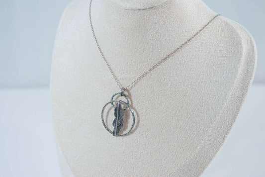 A handcrafted pendant with two interlocking rings and a delicate fern leaf at the center, suspended on a silver chain. Created by Inga Rozin