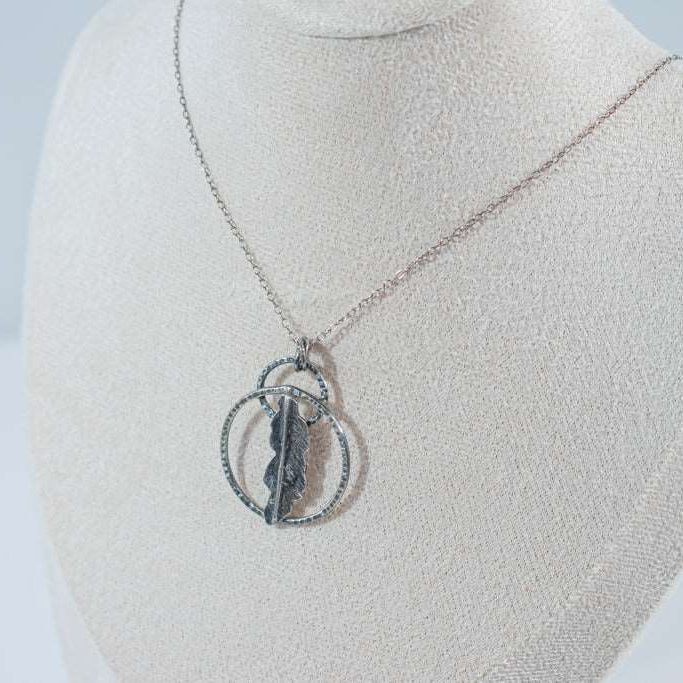 A handcrafted pendant with two interlocking rings and a delicate fern leaf at the center, suspended on a silver chain. Created by Inga Rozin