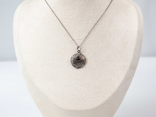 Handcrafted sterling silver maple leaf pendant with a deep red garnet stone, suspended on a delicate silver chain. Nature-inspired jewelry with intricate detailing and timeless elegance.