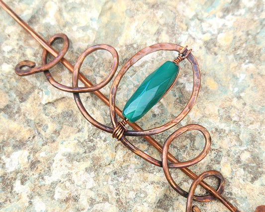 Copper hairpin with a green stone on a textured surface