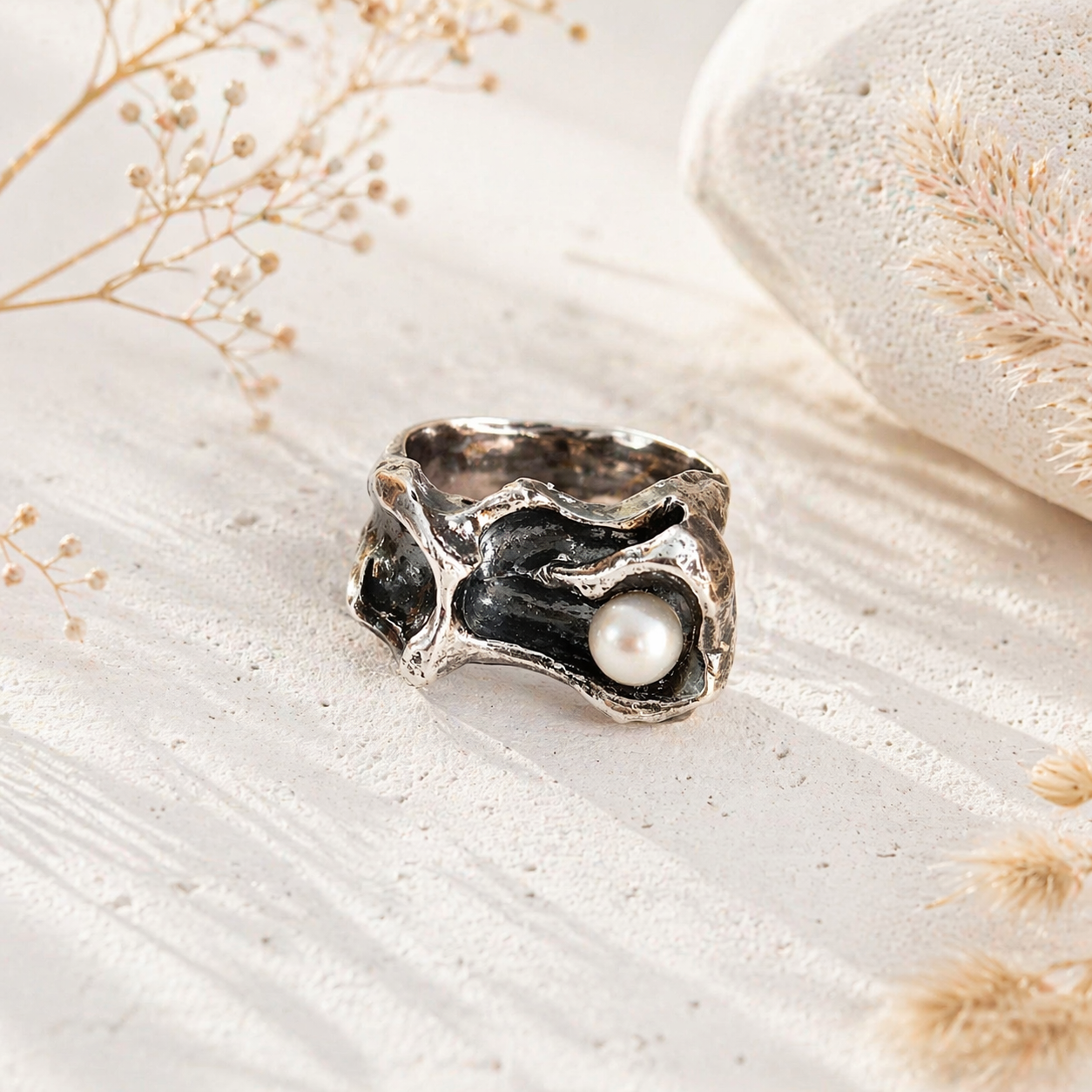 Silver ring with a pearl on a textured beige surface with dried flowers.