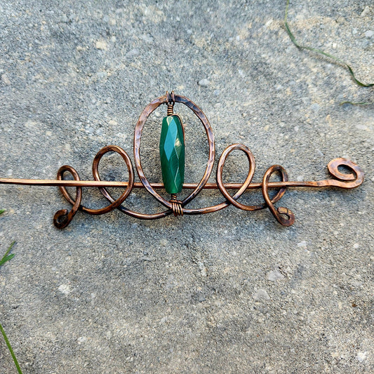 Copper hairpin with a green gemstone on a concrete surface