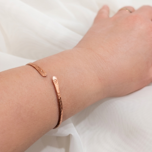 Copper bracelet on a wrist against a white fabric background