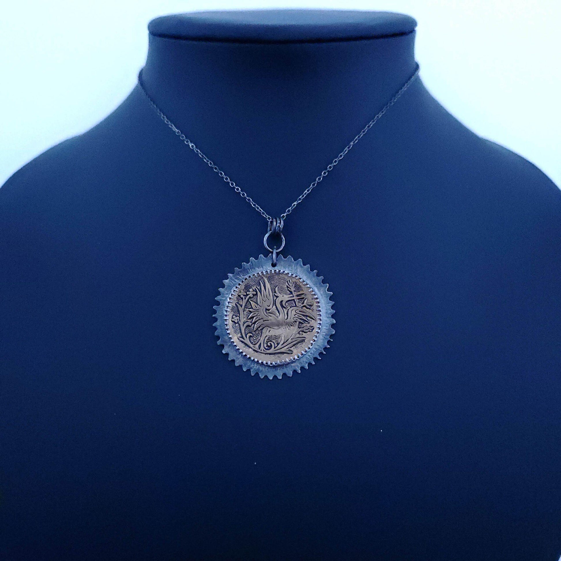 Unique pendant featuring a vintage bronze button with an intricately designed heron amid blooming flowers, set in a handcrafted sterling silver frame with a delicate floral motif.