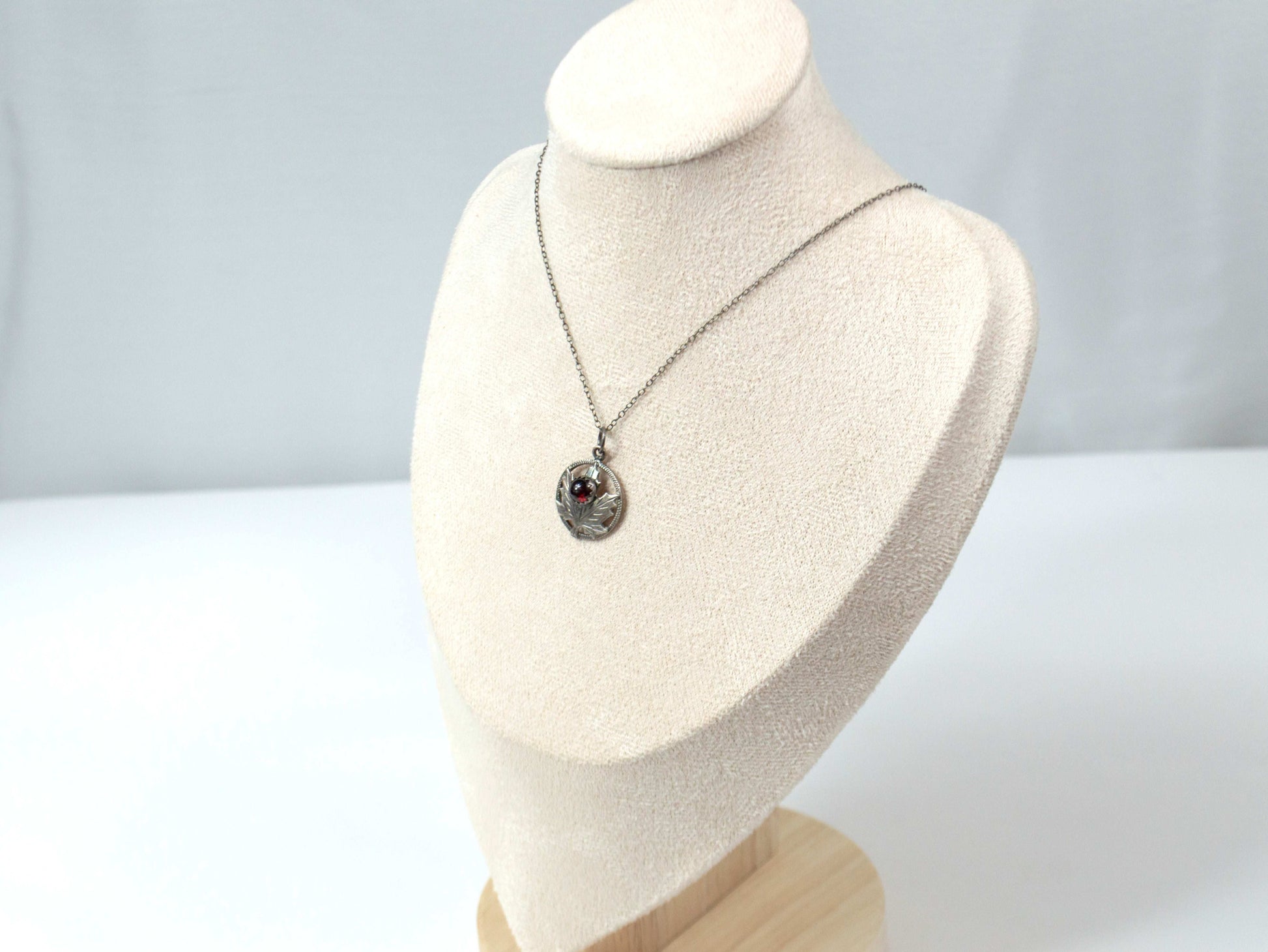 Handcrafted sterling silver maple leaf pendant with a deep red garnet stone, suspended on a delicate silver chain. Nature-inspired jewelry with intricate detailing and timeless elegance.