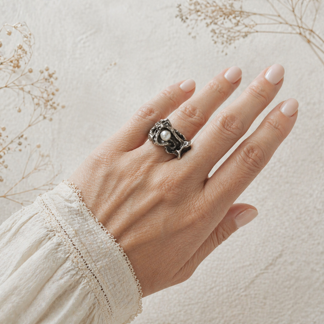 Hand wearing a bold ring with a pearl on a light background