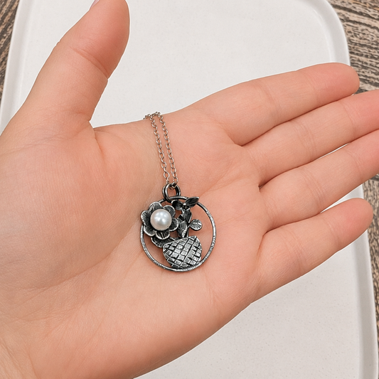 Hand holding a silver necklace with a pendant on a wooden surface