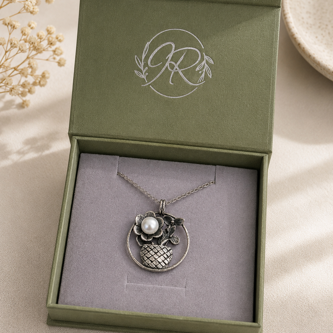 Silver necklace with a pendant in a green jewelry box on a light surface.