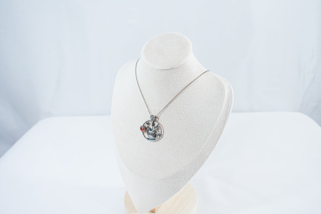 Handcrafted sterling silver pendant necklace featuring a textured teacup with tulips and a glowing Carnelian gemstone, inspired by spring and tea rituals.