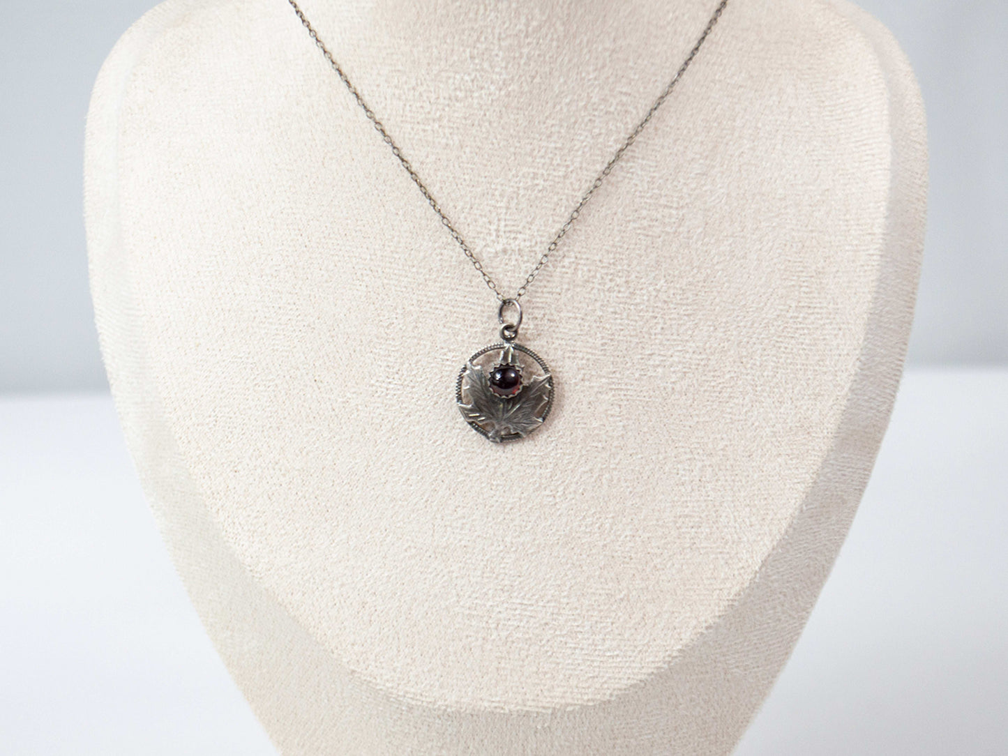Handcrafted sterling silver maple leaf pendant with a deep red garnet stone, suspended on a delicate silver chain. Nature-inspired jewelry with intricate detailing and timeless elegance.