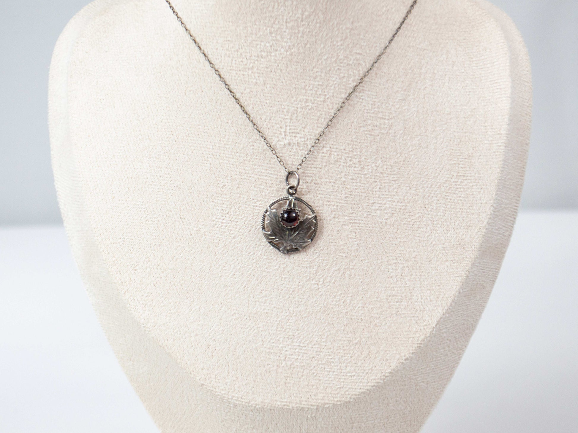 Handcrafted sterling silver maple leaf pendant with a deep red garnet stone, suspended on a delicate silver chain. Nature-inspired jewelry with intricate detailing and timeless elegance.