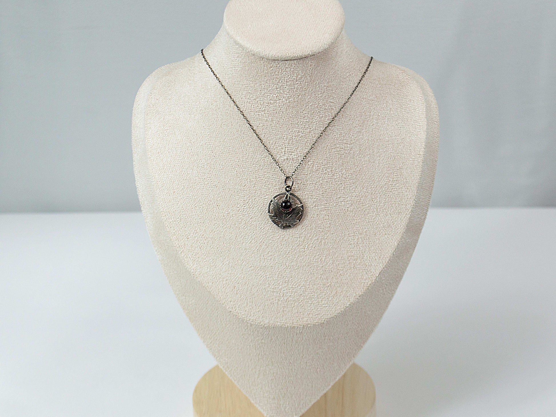 Handcrafted sterling silver maple leaf pendant with a deep red garnet stone, suspended on a delicate silver chain. Nature-inspired jewelry with intricate detailing and timeless elegance.