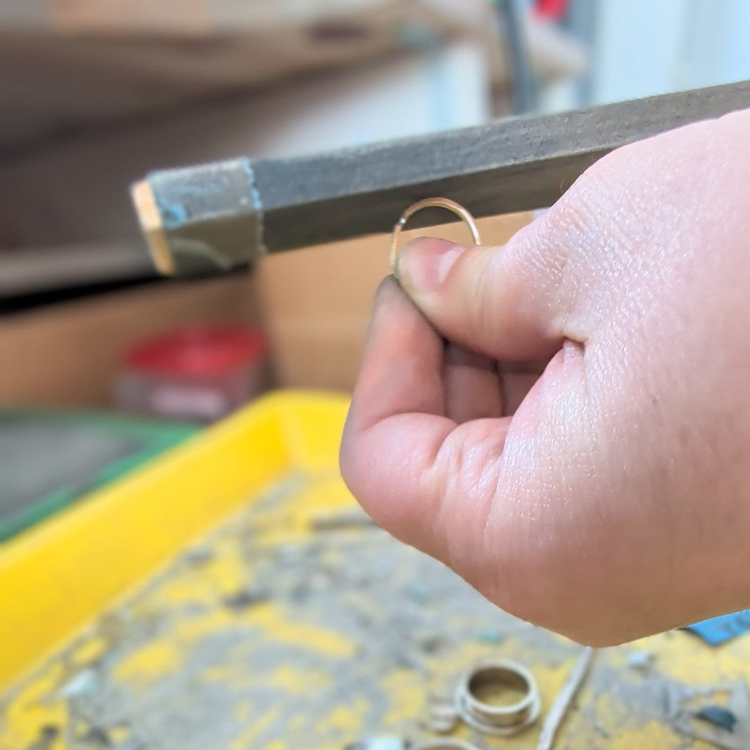 Hand holding a small metal ring with a blurred workshop background