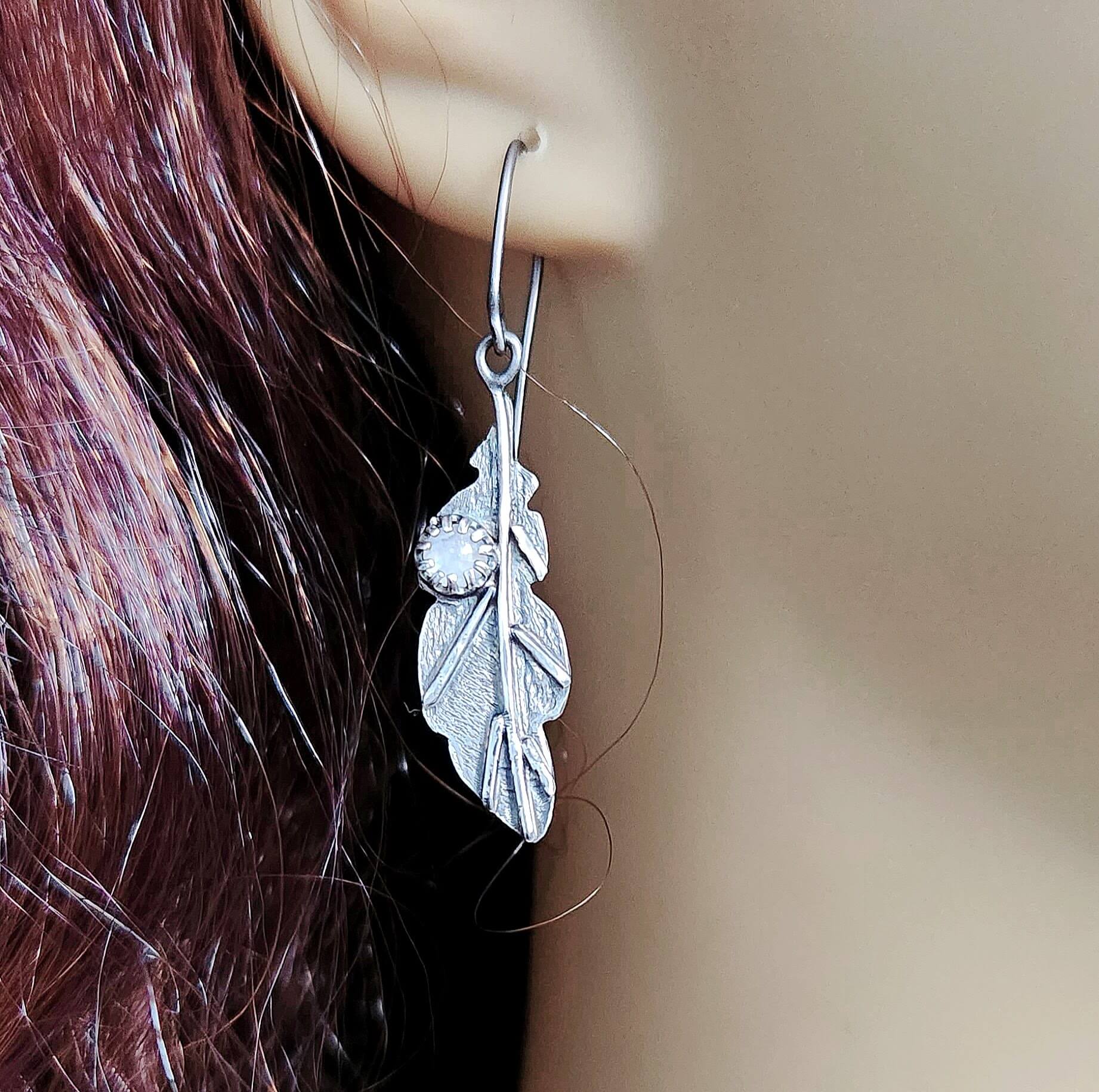 Sterling silver leaf earrings featuring shimmering rainbow moonstone accents.