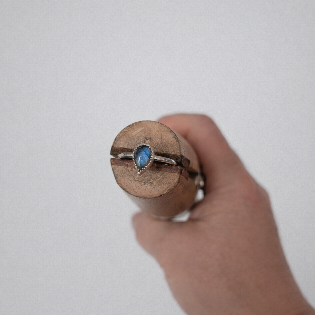 Hand holding a wooden cylindrical object with a ring featuring a blue stone against a plain background