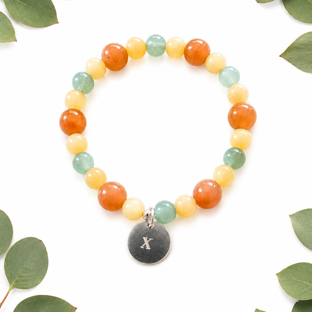 Multicolored beaded bracelet with a dark gray charm on a white background with green leaves.