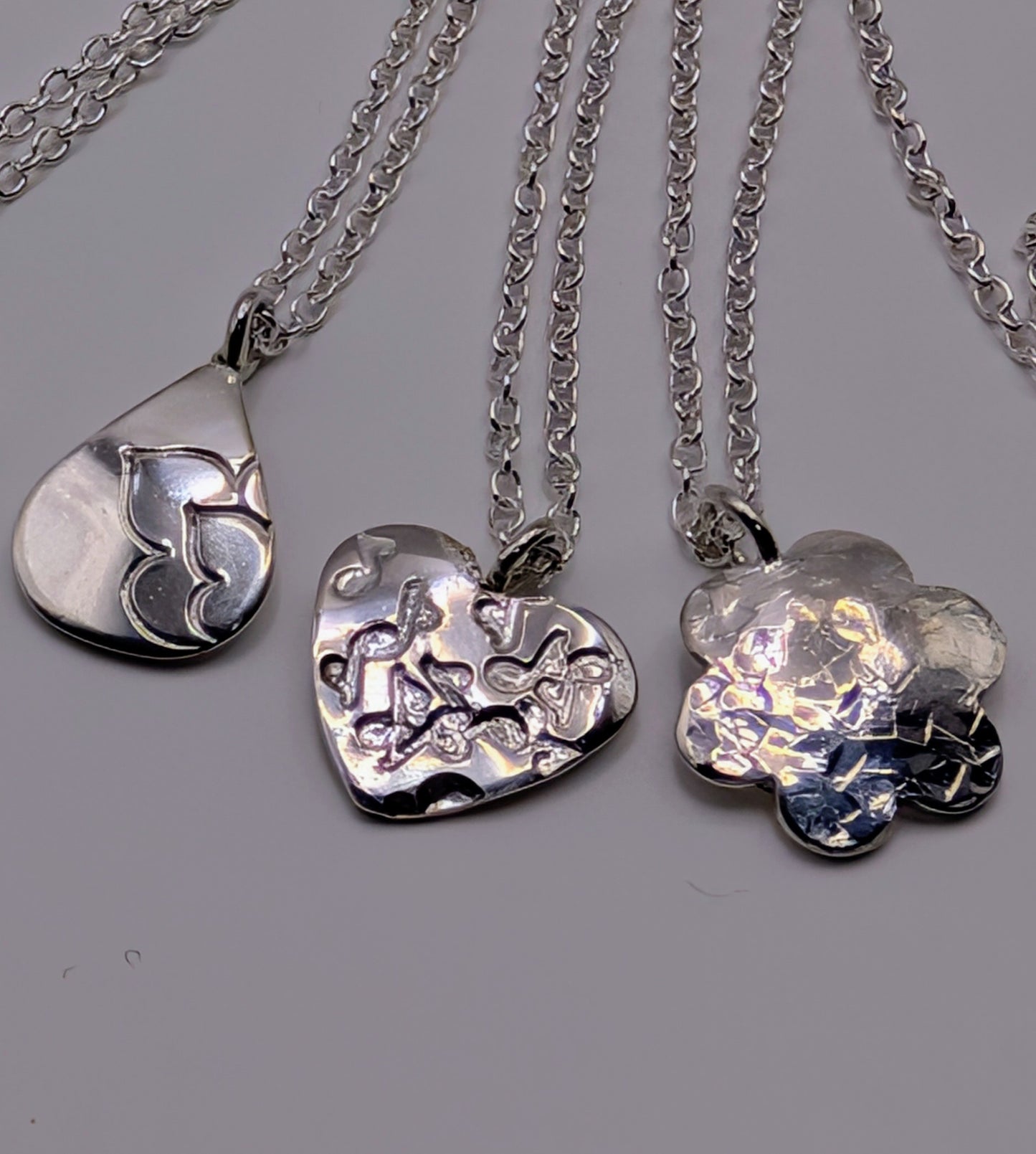 Three silver pendants on chains against a gray background