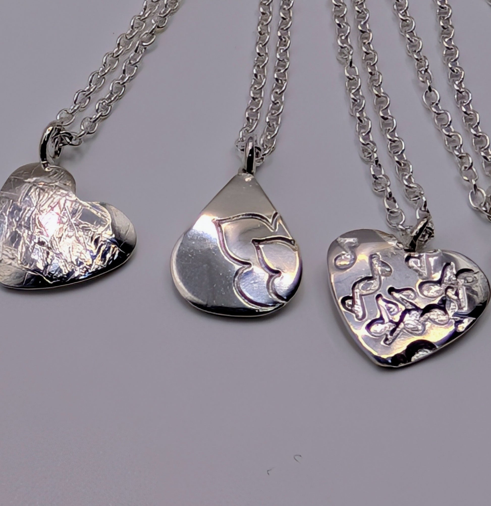Three silver pendants on chains against a gray background