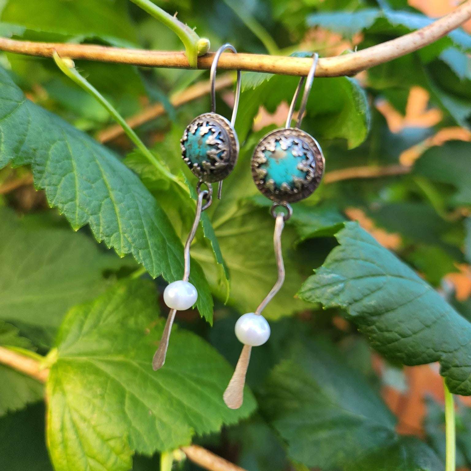 A pair of silver and turquoise dangle earrings with wavy silver accents, gracefully ending in smooth freshwater pearls for a balanced and elegant design.