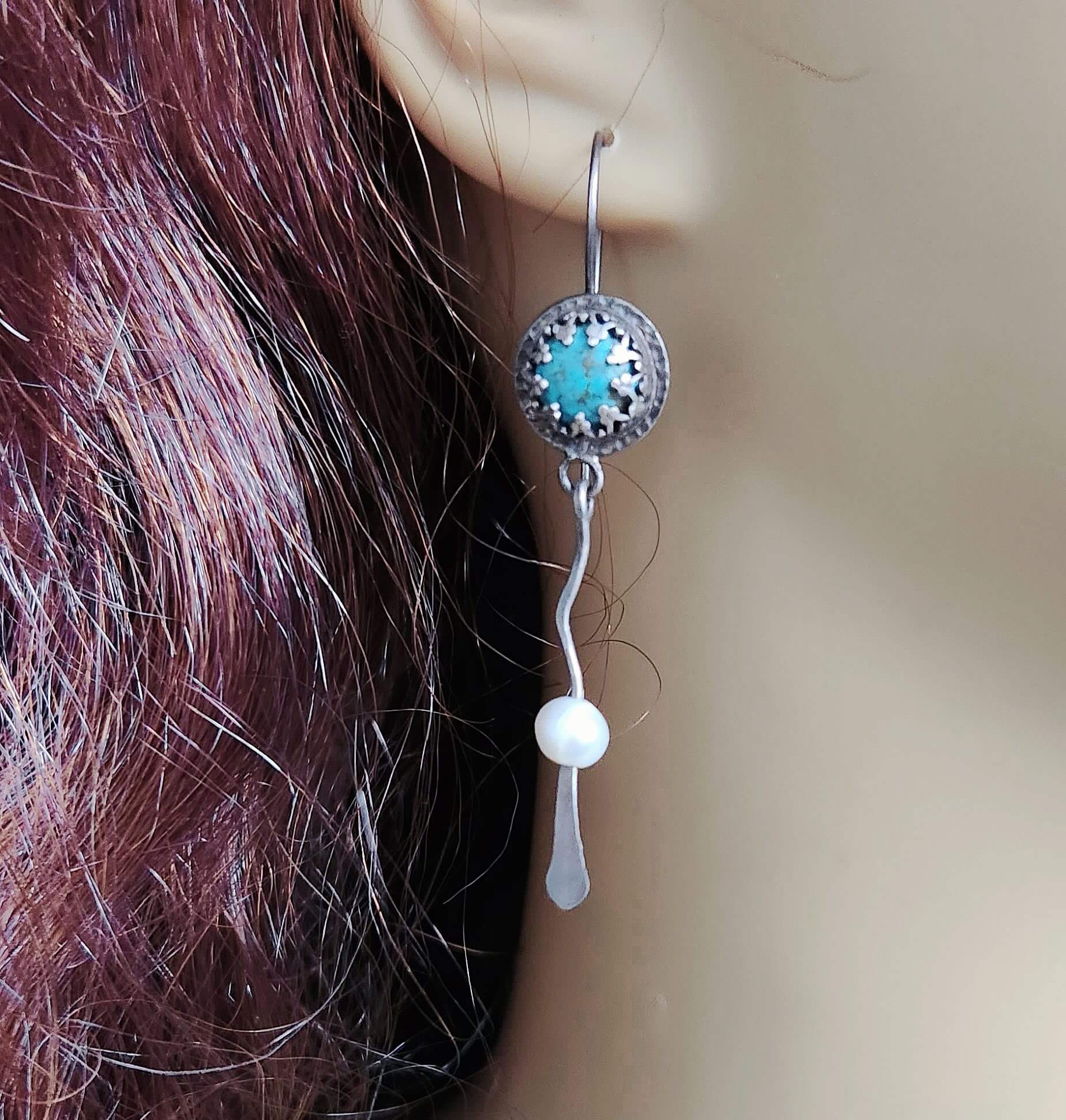 A pair of silver and turquoise dangle earrings with wavy silver accents gracefully ending in smooth freshwater pearls for a balanced and elegant design.